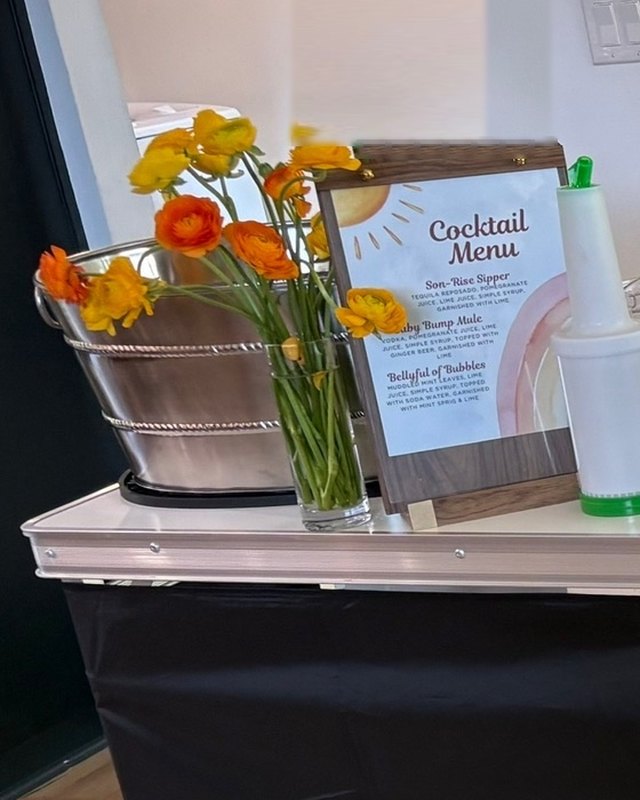 A printed cocktail menu standing on the bar beside fresh flowers
