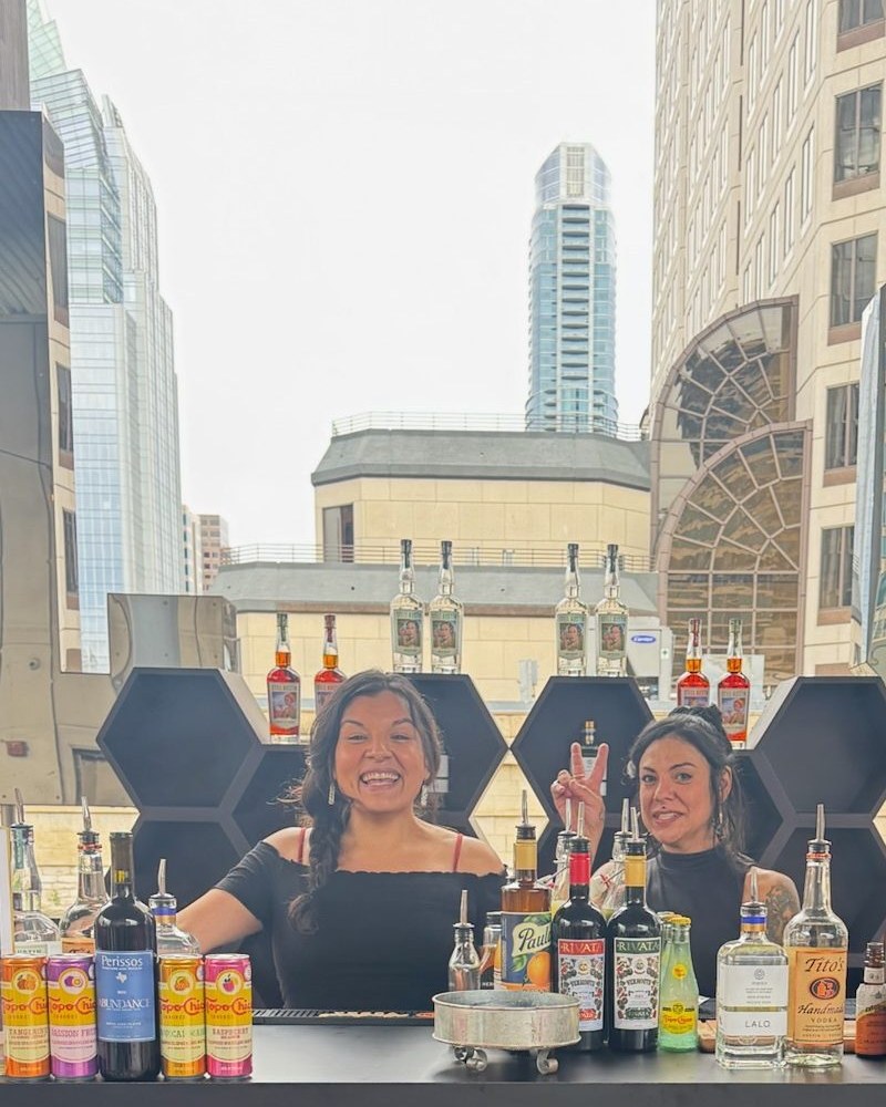 Two Mix Fix bartenders smiling behind the bar at a rooftop event in Austin